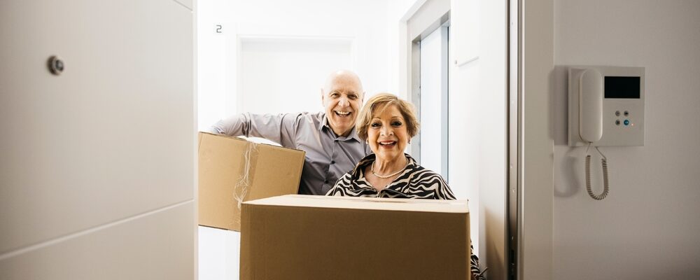 Smiling,Senior,Couple,Carrying,Cardboard,Boxes,While,Entering,Their,New Smiling,Senior,Couple,Carrying,Cardboard,Boxes,While,Entering,Their,New